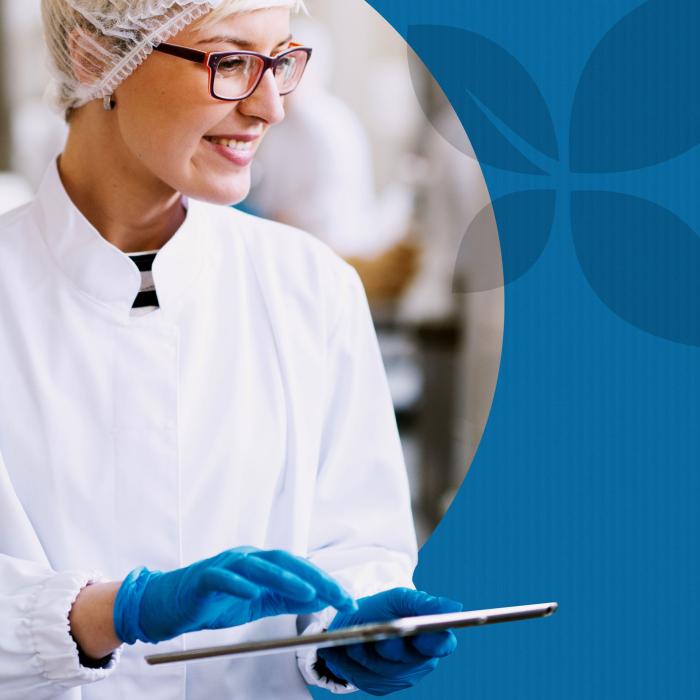 Female production facility employee wearing food-safe protective gear and gloves and carrying a tablet computer