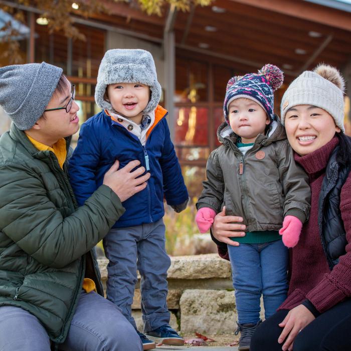 All of Us Hmong family of mom, dad and two young sons outdoors in winter clothing enjoying a late fall day