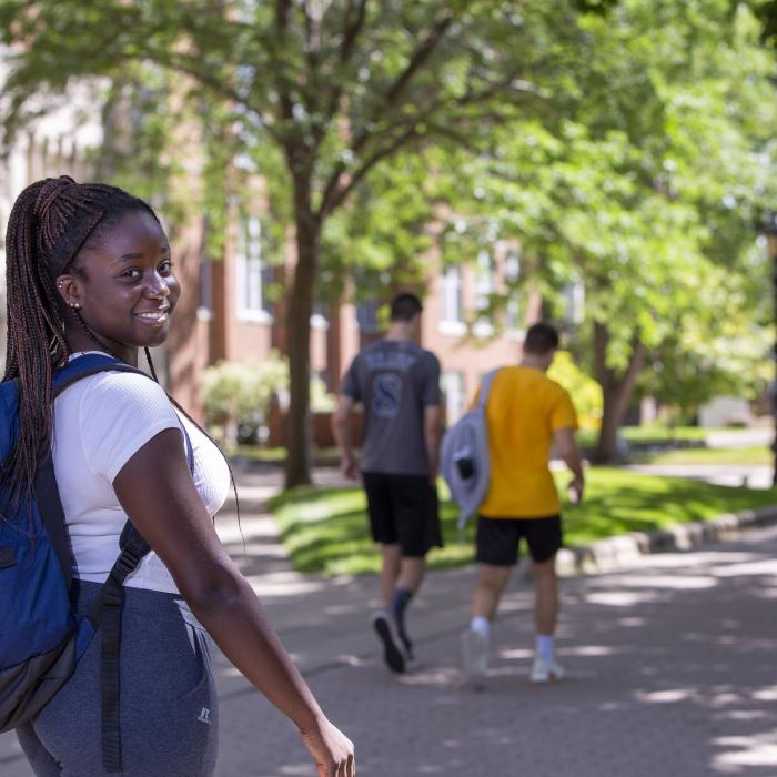 Student walking on campus, looking over her right shoulder and smiling