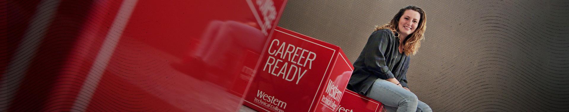 Panoramic photo of Western Technical College student sitting on a Western red box with two other red boxes in the foreground