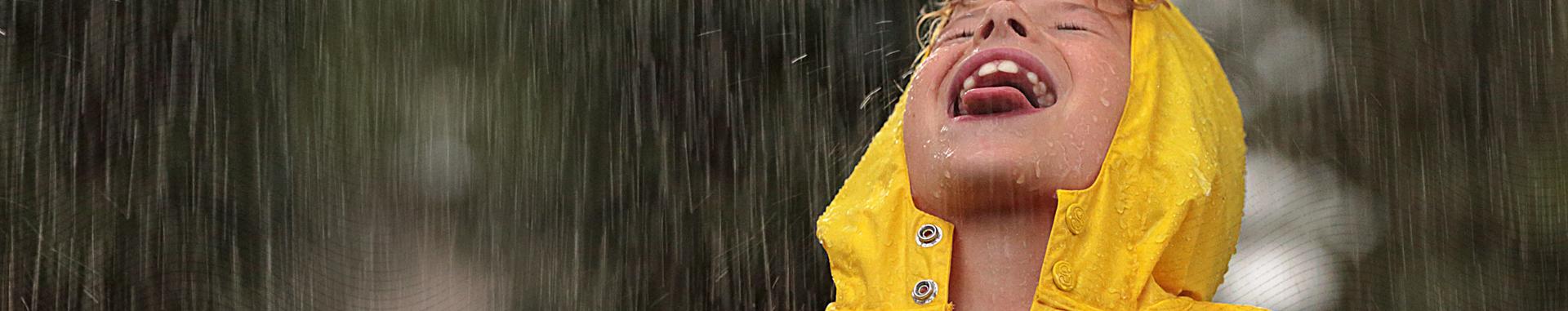 Panoramic image of the face of a boy playing in the rain wearing a yellow hooded raincoat from health insurer video