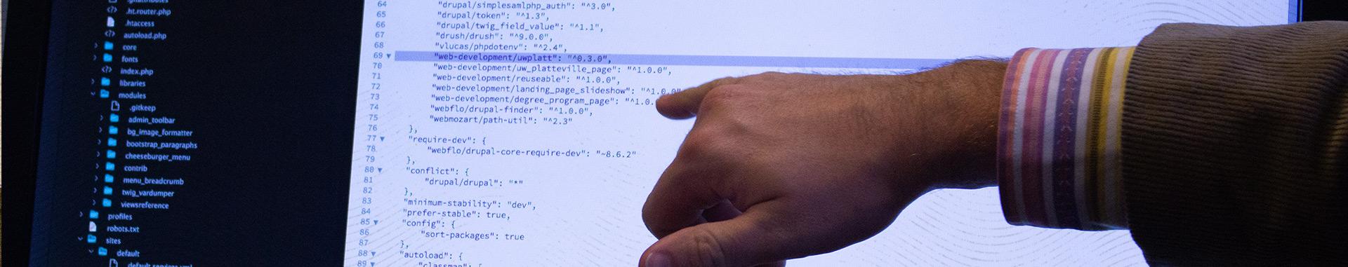 Hand and forearm of a Male Vendi employee pointing out specific web development code on a computer screen