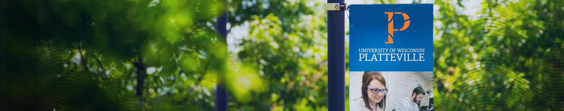 Panoramic view of University of Wisconsin-Platteville banner hanging among green trees on the UWP campus