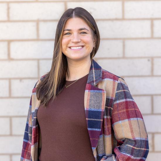 Headshot of woman smiling in a flannel with a light tan brick background