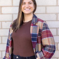 Headshot of woman smiling in a flannel with a light tan brick background