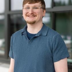 Man in a blue shirt smiling with a window in the background